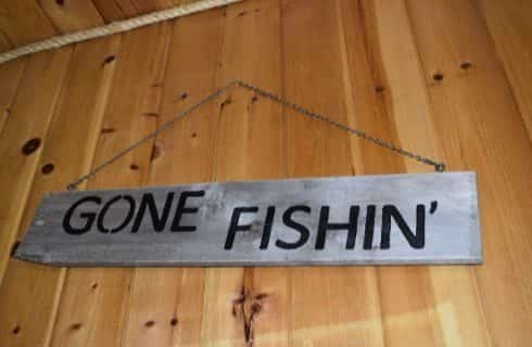 Large gray wood plank sign that says Gone Fishin' hanging on a light wood paneled wall