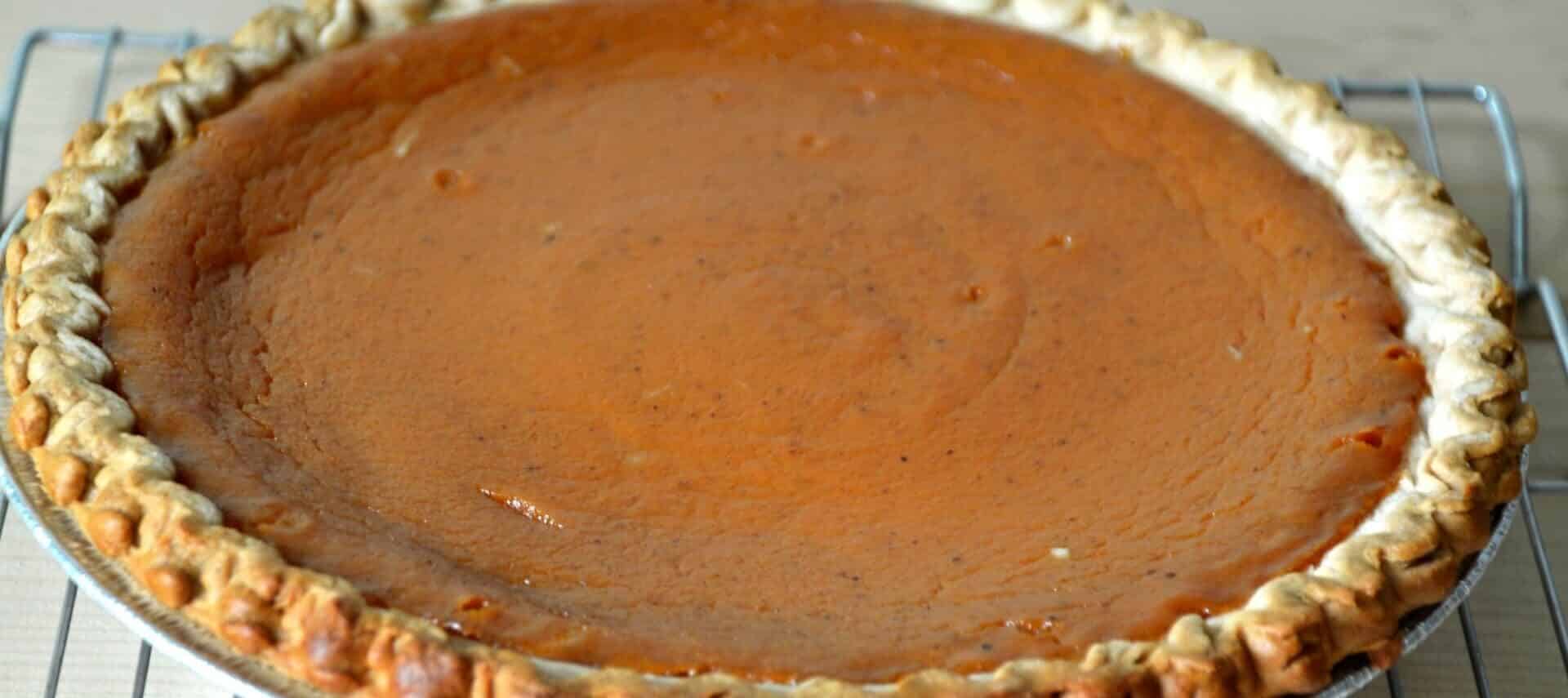 Pumpkin pie with browned crust sitting on silver cooling rack.