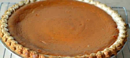 Pumpkin pie with browned crust sitting on silver cooling rack.