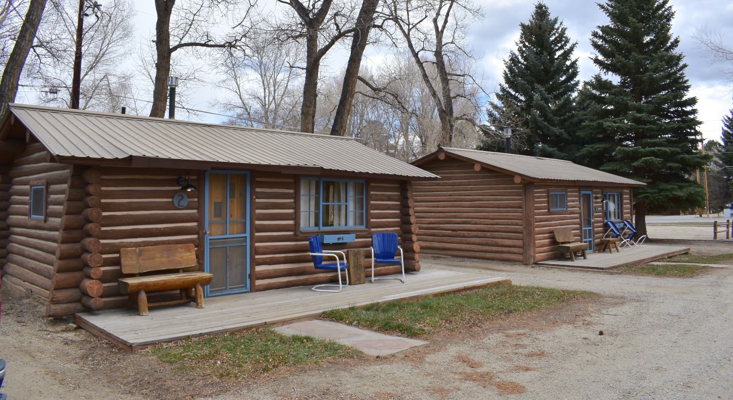 Multiple wooden cabins with blue painted door and trim surrounded by large evergreen trees