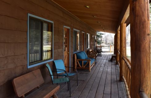 Close up view of a lodge's large porch with wooden furniture and metal chairs
