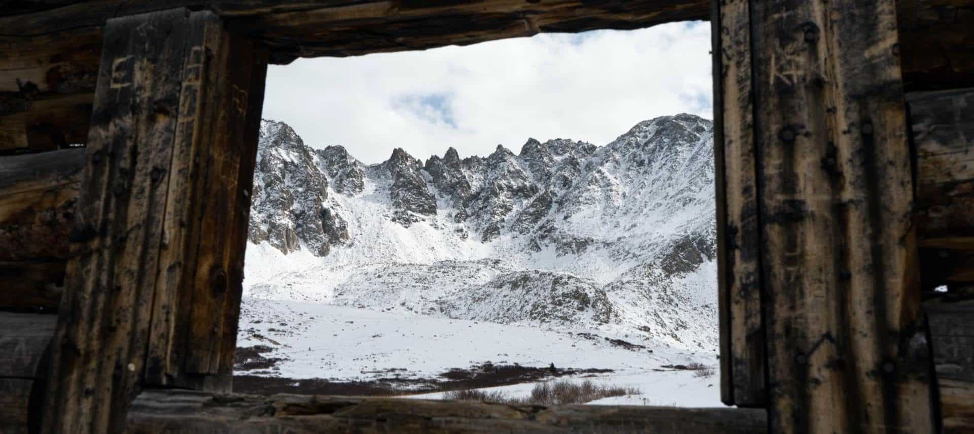 View of snow covered mountains through a window from inside a wood cabin