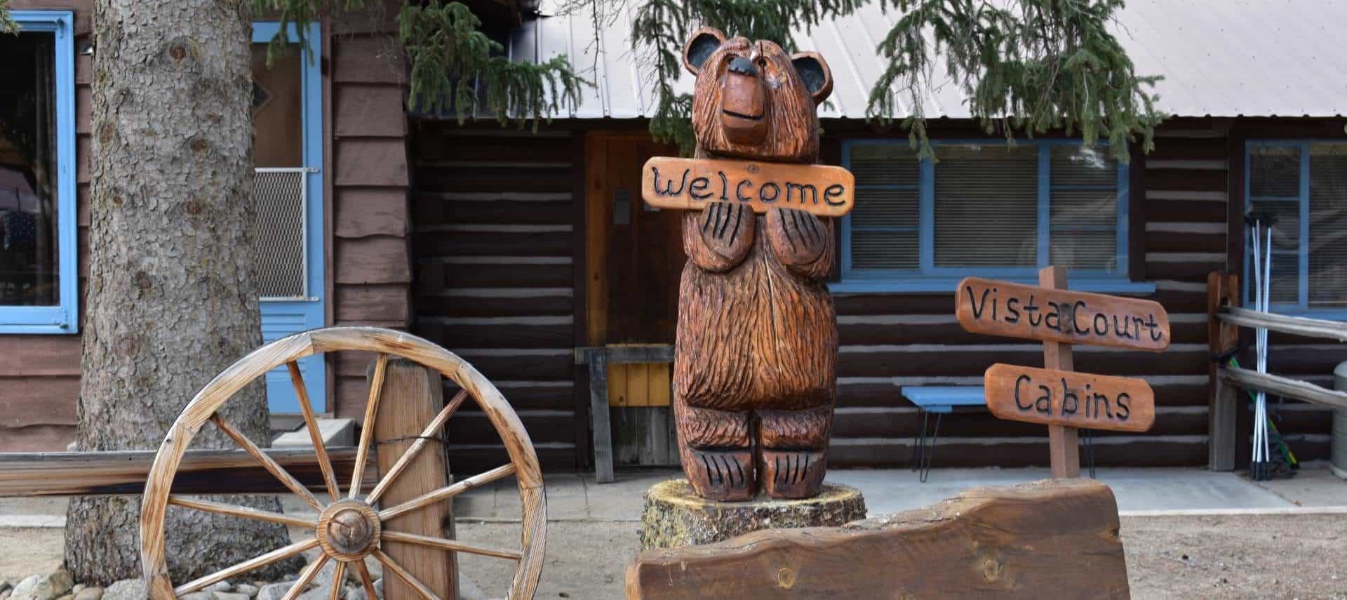 Wooden cottage with blue painted door and trim with a carved wooden bear holding a welcome sign