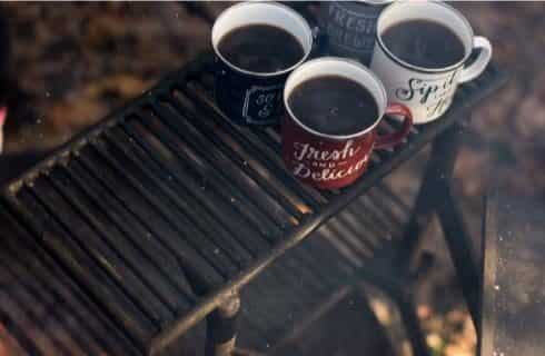 Four coffee cups filled with coffee sitting on top rack of fire pit grill